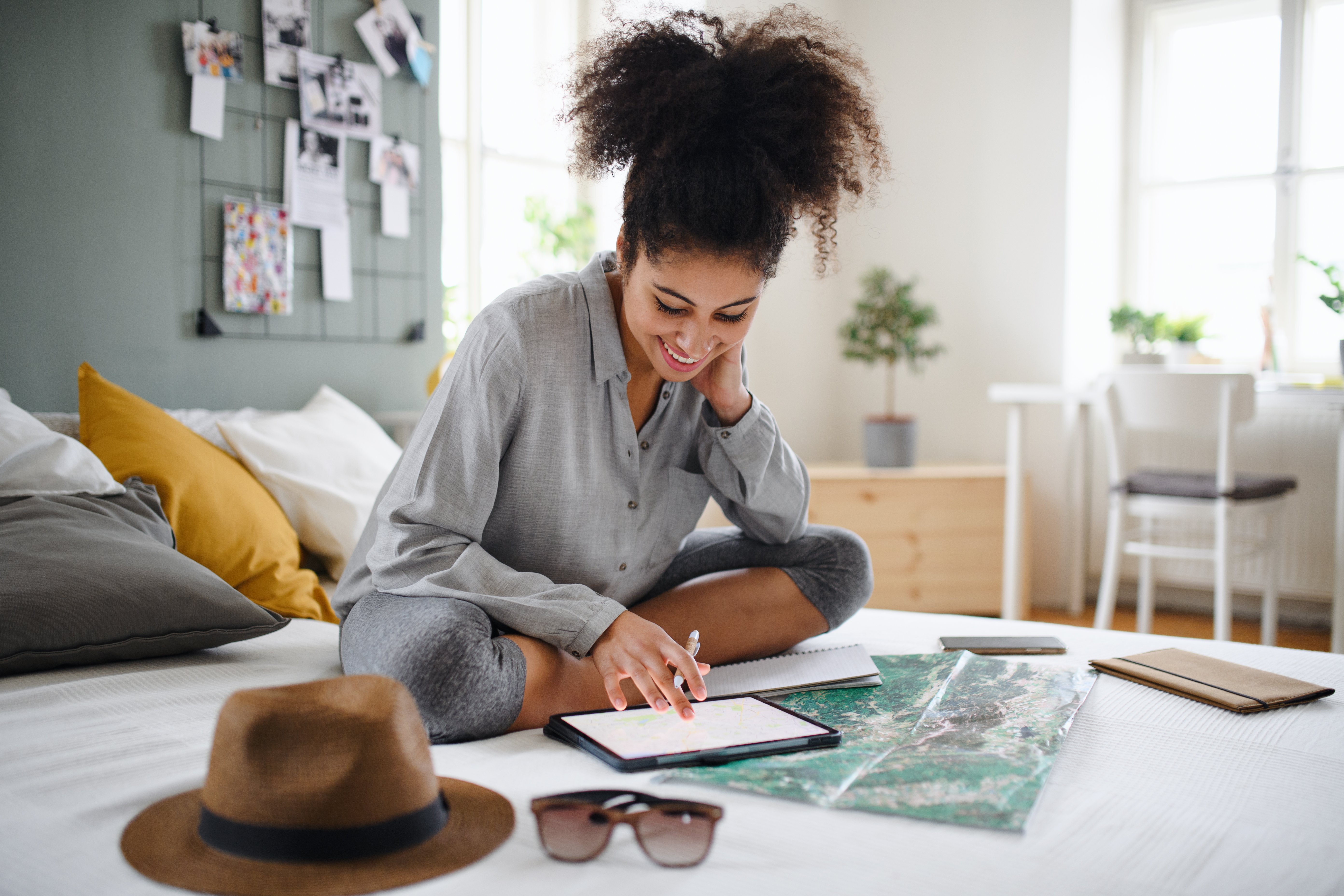 Happy young woman indoors at home, using a tablet and map to plan her trip.